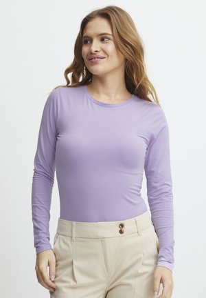 Blusa de manga larga púrpura hecha de un material suave y elástico. Escote redondo y diseño ajustado, combinada con pantalones beige de talle alto que presentan detalles de botones.