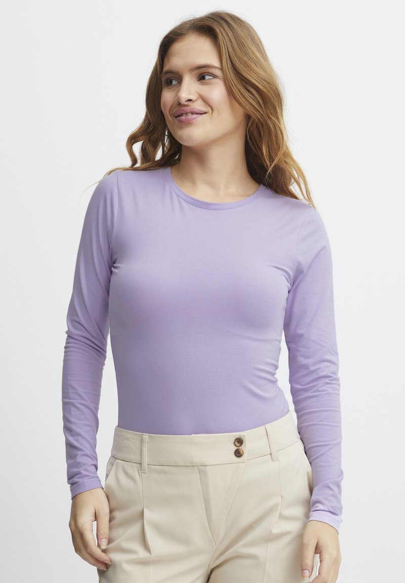 Paarse top met lange mouwen van een gladde, rekbare stof. Ronde halslijn en een getailleerd ontwerp, gecombineerd met beige hoge taillebroeken met knoopaccenten.