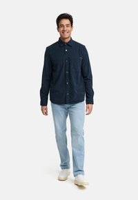 Mørkeblå skjorte med knappestolpe og brystlomme, kombinert med lyseblå jeans og hvite joggesko, med en avslappet passform og teksturert stoff.