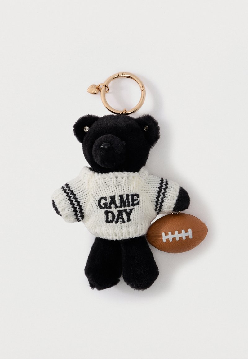 Sort tøjdyrs-nøglering iført hvid strikket sweater med teksten "GAME DAY", der holder en lille brun fodbold på hvid baggrund.