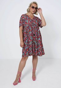 Red floral dress with short sleeves and a V-neck, featuring blue and pink accents. Paired with pink platform heels and sunglasses.