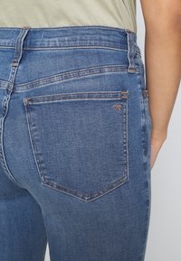 Jeans de mezclilla azul con un diseño ajustado, cintura de altura media y un estilo clásico de cinco bolsillos con detalles de costura en contraste.