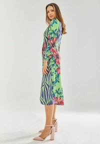 Floral and zebra print dress in green, featuring long sleeves and a knee-length design. Worn with light pink block-heeled shoes.