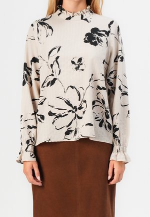 Langærmet bluse i beige stof med sort blomsterprint, flæsekrave og rynkede manchetter. Sammen med en brun nederdel.