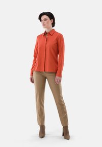Orange button-up shirt with long sleeves, paired with beige fitted pants and tan high-heeled boots. Simple design, smooth texture.