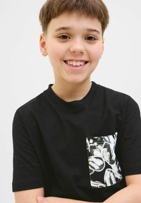 Juoda medvilnės marškinėliai su kišenę, padengtą baltu gėlių raštu. Trumpomis rankovėmis ir apvaliu iškirpimu. Lygus paviršius.