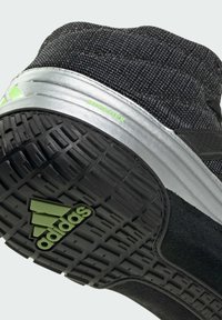 Black athletic shoe with a textured fabric upper, silver midsole, and rugged black outsole featuring green accents and logo.