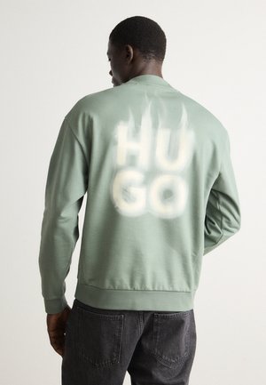 Felpa verde con maniche lunghe e scollatura rotonda. "HUGO" stampato in bianco sulla schiena con un effetto testurizzato. Vestibilità classica.