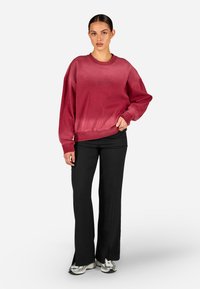 Bordový skrátený sveter s rebrovanými manžetami, s jemným logom. V kombinácii s čiernymi širokými nohavicami a metalickými teniskami.