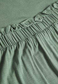 Vihreä kangas, jossa on kerrostettu ripsiväritys sauman varrella, ja joka omaa sileän tekstuurin ja hieman laskeutuvan ulkonäön.