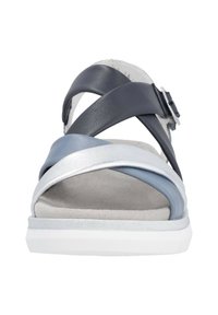 Das Schuhwerk hat synthetische Riemen in Marineblau, Silber und Hellblau mit einem geschwungenen Design. Die strukturierte Sohle ist weiß mit einer weichen, grauen Einlegesohle.
