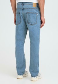 Jeans de mezclilla azul claro con un diseño de pierna recta, que cuentan con dos bolsillos traseros y un parche de cuero marrón en la cinturilla.