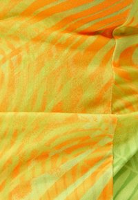 Textil s živým abstraktním vzorem v oranžových a zelených odstínech, hladkou texturou a lehkým, splývavým designem.