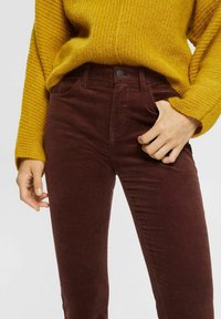 Burgundy corduroy high-waisted pants with a button closure and front pockets, paired with a textured mustard yellow knit sweater.