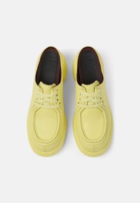 Scarpe in pelle gialla con una texture liscia, punte rotonde e dettagli cuciti. Presentano lacci abbinati e una soletta scura in un colore contrastante.