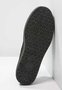 Suola di scarpa in gomma nera con un motivo testurizzato che presenta forme esagonali e un logo circolare al centro. Design piatto e antiscivolo.