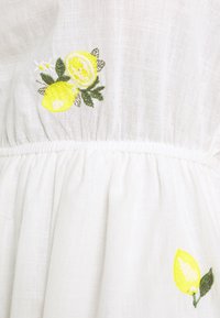 Weißes Leinenkleid mit gelber Zitronenbestickung und grünen Blättern. Strukturierten Stoff mit gerafftem Taillenrand und sanft fließendem Rock.