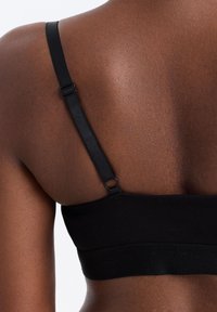 Nahaufnahme des oberen Rückens einer dunkelhäutigen Person, die ein schwarzes verstellbares BH-Träger und -Band trägt.