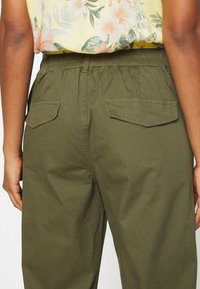 Kalhoty olivové barvy s elastickým páskem, dvěma zadními kapsami a volným střihem. Texturovaný bavlněný materiál; hladký povrch.