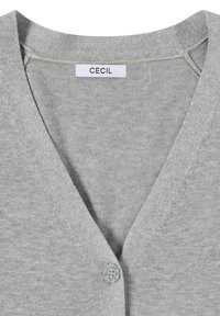 Cardigan en maille gris clair avec col en V, un seul bouton visible et une étiquette blanche portant l'inscription "CECIL" au niveau du col.
