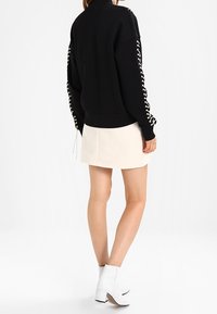 Mustapaita, jossa on nyörityksellä varustetut hihat, yhdistettynä vaalean kermaiseen hameeseen. Valkoiset nilkkurit täydentävät asukokonaisuuden. Suuret ja sileät tekstuurit näkyvät.