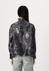 Blusa trasparente con stampa serpente nera e grigia, orlo arricciato e colletto alto. Presenta maniche lunghe con polsini aderenti.