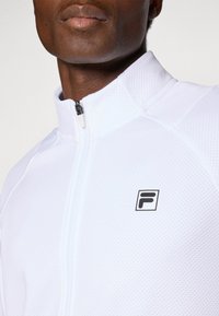 Giacca bianca con zip, in un tessuto testurizzato e con un logo nero sul petto. Il design presenta un collo alto con un dettaglio della zip liscia.