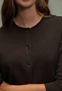 Bruine, getextureerde gebreide cardigan met een ronde hals, knoopsluiting aan de voorkant met vier zwarte knopen en driekwart mouwen.