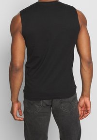 Camiseta sin mangas negra de algodón, con escote redondo y corte relajado, combinada con jeans de mezclilla gris oscuro.