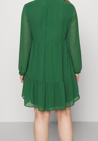 Zielona, warstwowa sukienka z długimi rękawami i falbaną na dole. Wykonana z lekkiego, przejrzystego materiału, z okrągłym dekoltem i gładką fakturą.