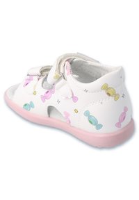 Białe sandały z pastelowymi wzorami cukierków, różową podeszwą i dwoma rzepami. Charakteryzują się otwartymi bokami i teksturowanym wnętrzem dla większego komfortu.