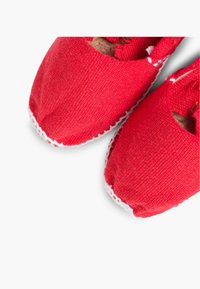 Scarpe slip-on rosse in tela con punta rotonda, con cuciture bianche dettagliate lungo la suola e una morbida fodera interna beige.