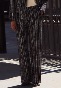 Svarta och vita rutiga byxor i texturerad tyg, med en vida bendesign och subtila metalliska detaljer.