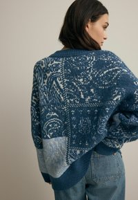 Blauer gemusterter Strickpullover mit einer lockeren Passform, der verschiedene Blautöne und filigrane Designs aufweist. Rippenbündchen und -saum.