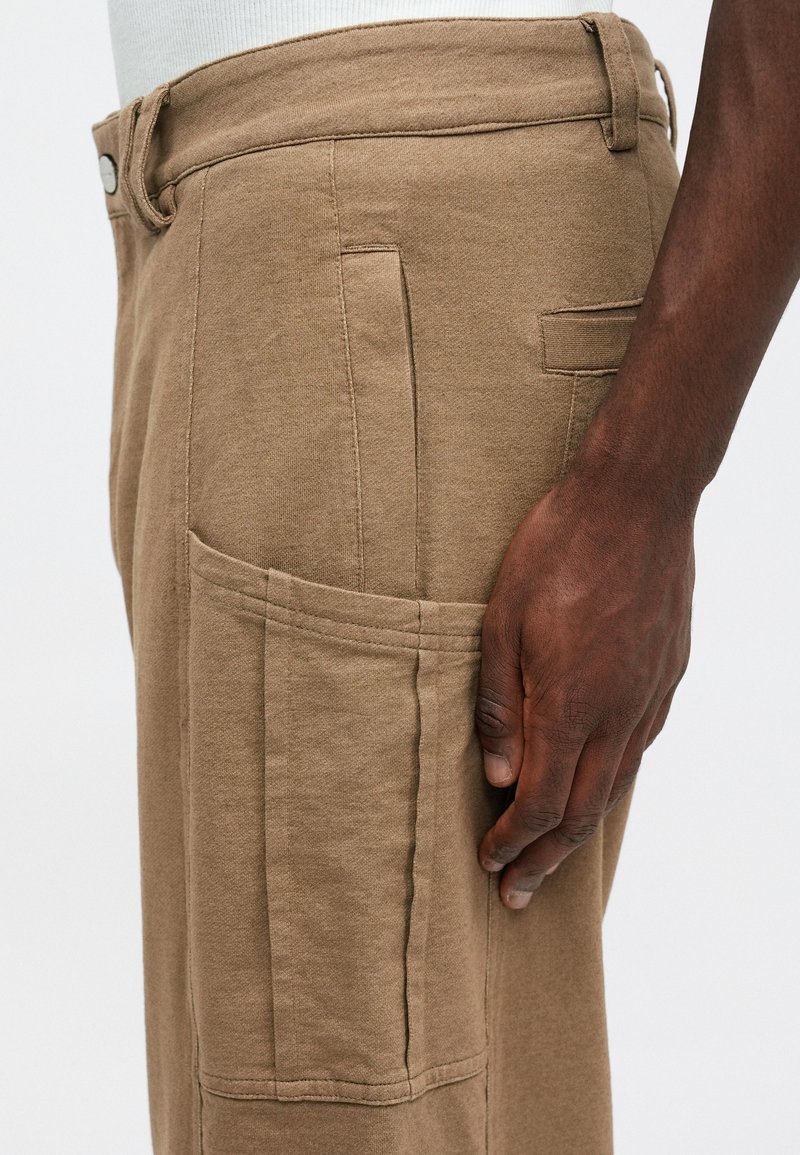 Pantalon cargo kaki en tissu doux, doté d'une poche latérale avec un rabat et des détails de couture visibles.