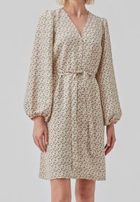 Beige Kleid mit Blumenmuster, Wrap-Design, langen Puffärmeln und einem abnehmbaren Bindegurt in der Taille, aus leichtem Stoff.