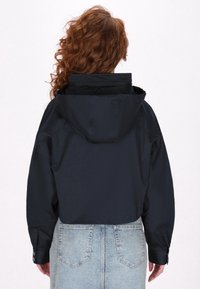 Marineblauwe hoodiejack met een cropped ontwerp, voorzien van lange mouwen en verstelbare manchetten, gedragen met een lichtblauwe denimrok.