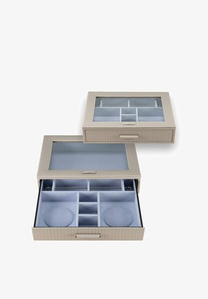 Organisateur de bijoux beige avec couvercle transparent, tiroir ouvert montrant plusieurs compartiments et coussins rembourrés pour montres à l'intérieur.