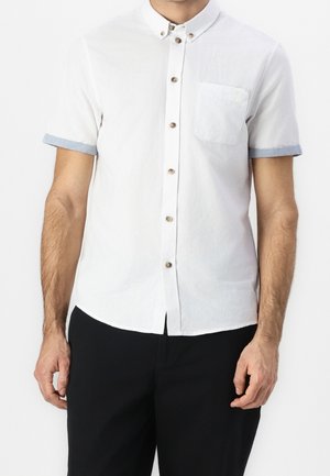 Wit overhemd met korte mouwen, een button-down kraag, lichtblauwe opgerolde manchetten, een borstzak en bruine knopen. Soepele katoenen textuur.