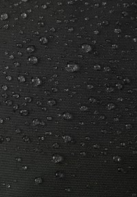 Czarna teksturowana tkanina z kroplami wody na powierzchni, prezentująca wodoodporny materiał zaprojektowany do odpychania wilgoci.