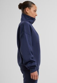 Felpa zip con collo alto di colore blu navy, vestibilità over, con polsini e orlo a costine, realizzata in morbido tessuto misto cotone.