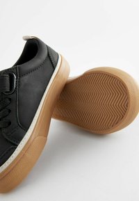 Svarta lädersneakers med gummisula som har ett texturerat fiskbensmönster. Taperad form och kontrasterande vit sömnadsdetalj.