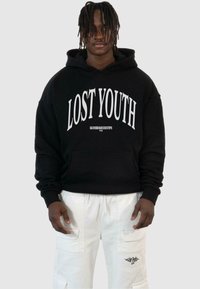 Svart huvtröja med "LOST YOUTH" i vit text, med framfickor och ribbad mudd. Tillsammans med vita cargoshorts med accentstickningar.