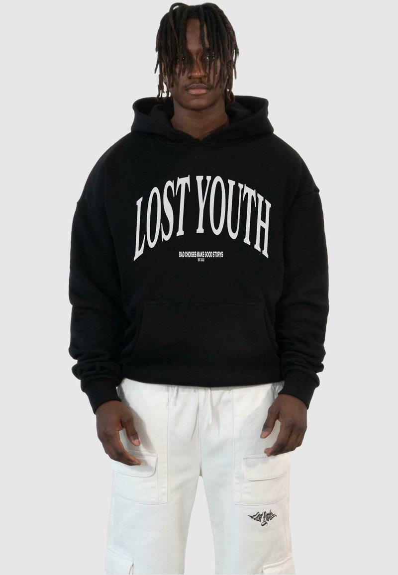 Svart huvtröja med "LOST YOUTH" i vit text, med framfickor och ribbad mudd. Tillsammans med vita cargoshorts med accentstickningar.