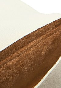 Weißer strukturierter Lederbeutel mit einem weichen braunen Innenraum. Verfügt über klare Linien und eine geräumige Öffnung, die die kontrastierenden Materialien zur Geltung bringt.