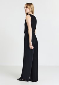 Combinaison noire sans manches avec un corsage ajusté, un design à jambes larges et une texture lisse. Style minimaliste avec une silhouette propre et élégante.