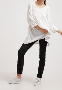Løs pasform hvid bluse med lange ærmer, tekstureret stof; parret med sorte slim-fit bukser og lysegrå sneakers.