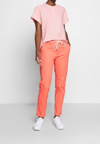 Top rosa chiaro a maniche corte con righe verticali e patta dei bottoni, abbinato a pantaloni arancioni con cordoncino e sneakers bianche.