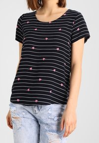 T-shirt à rayures noires avec motifs de cœurs roses, manches courtes et encolure ronde, assorti à un jean bleu clair déchiré.