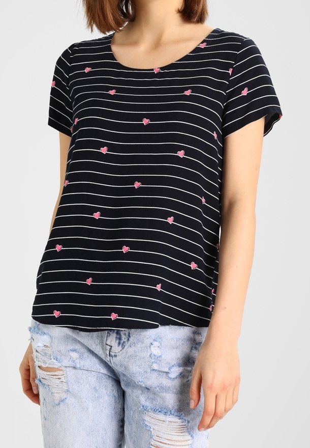 T-shirt à rayures noires avec motifs de cœurs roses, manches courtes et encolure ronde, assorti à un jean bleu clair déchiré.